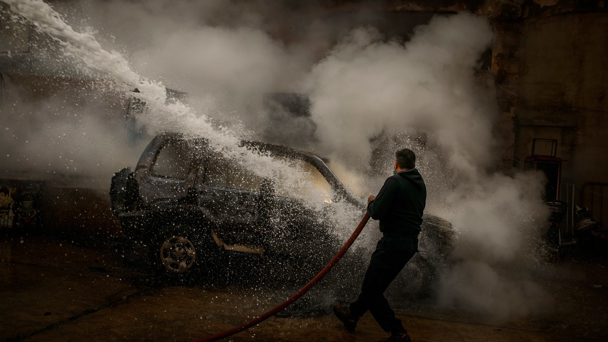 A member of the Lebanese Civil Defense extinguishes a police car that was set on fire by protesters in Tripoli.