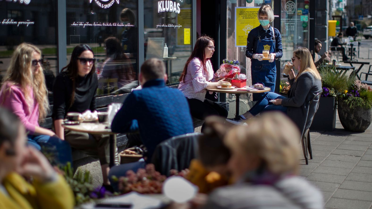 A waitress wears a face mask while serving customers at a restaurant in Vilnius, Lithuania, on April 30. The Lithuanian government extended the country's nationwide lockdown until May 11, but it gave the green light for museums, libraries, outdoor cafes, hairdressers, beauty salons and shopping mall retail stores to reopen. 