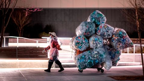 A woman wearing a face mask and a plastic bag pulls a cart loaded with bags of recyclables through the streets of Lower Manhattan in April.