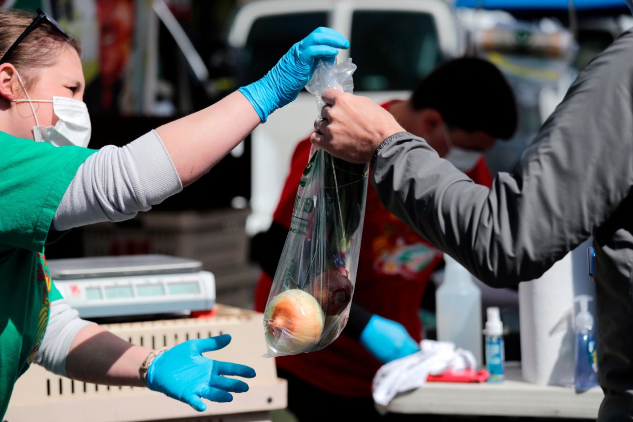 Farmer Samantha Alvarez, left, hands a bag of onions to a customer at the West Seattle Farmers Market on May 3. Farmers markets in Seattle reopened with guidelines that include fewer vendors allowed, a limited number of customers, and additional hand-washing and sanitizing stations.