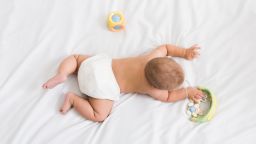 Small baby in diaper lying on his belly on white bed with toys