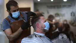 A hairdresser wears a face mask as he cuts the hair of a client at the hairdressing salon 'Erhan's Gentlemen Friseursalon' in Dortmund, western Germany, on May 4, 2020, amid the new coronavirus Covid-19 pandemic. - Since May 4, 2020, hairdressing salons in federal state of Baden-Wuerttemberg can re-open under strict rules for hygiene and distance. (Photo by Ina FASSBENDER / AFP) (Photo by INA FASSBENDER/AFP via Getty Images)