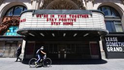 A cyclist in facemask rides past the Million Dollar Theater, closed due to the coronavirus pandemic, with words on the marqee calling for togetherness and positivity, on May 4, 2020 in Los Angeles, California. - California governor Gavin Newsom earlier today announced the gradual reopening of the state later this week as dismal US employment figures are expected with the release of figures Friday May 8 for April's US jobs report, as 30 million Americans filed for unemployment in the last six weeks. (Photo by Frederic J. BROWN / AFP) (Photo by FREDERIC J. BROWN/AFP via Getty Images)