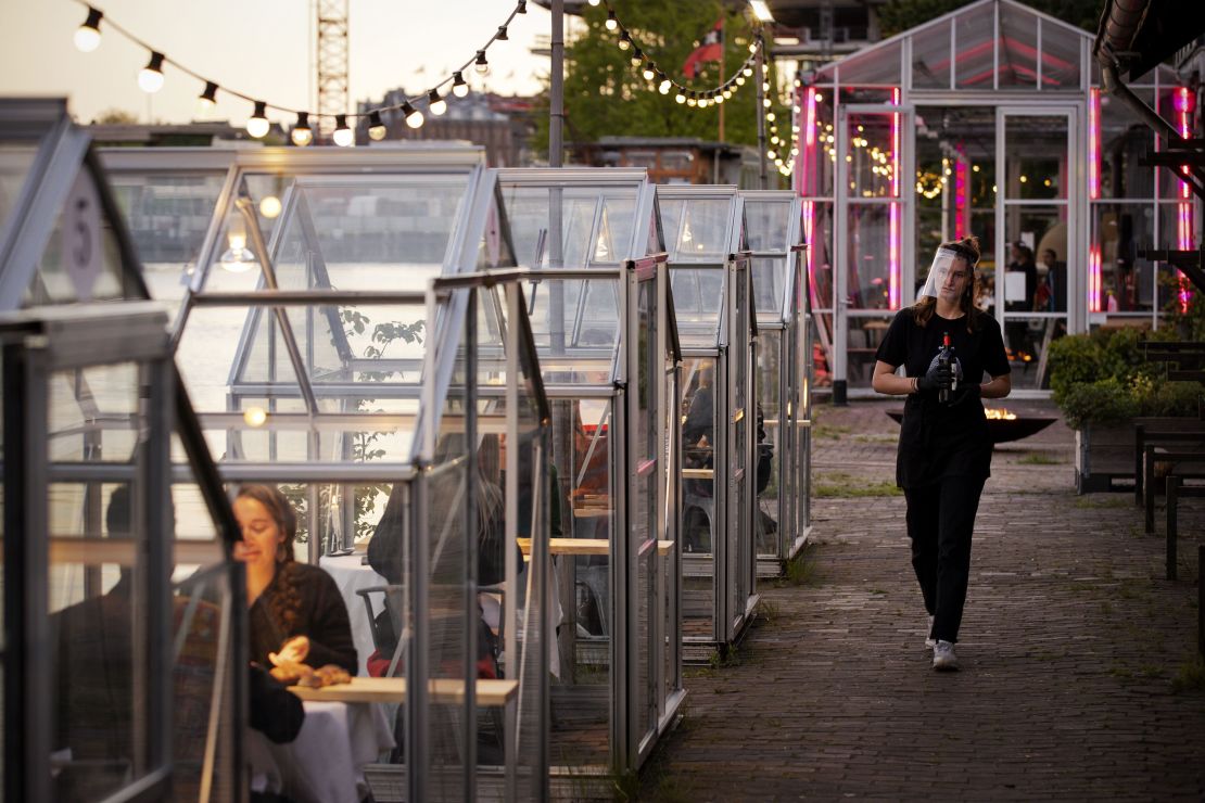 A waitress wearing a protective face shield arrives to serve wine to friends having dinner in a so-called quarantine greenhouses in Amsterdam, on May 5, 2020 as the country fights against the spread of the COVID-19, the novel coronavirus. 