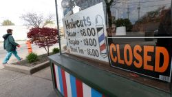 A woman walks past a closed barber shop, Wednesday, May 6, 2020, in Cleveland. (AP Photo/Tony Dejak)