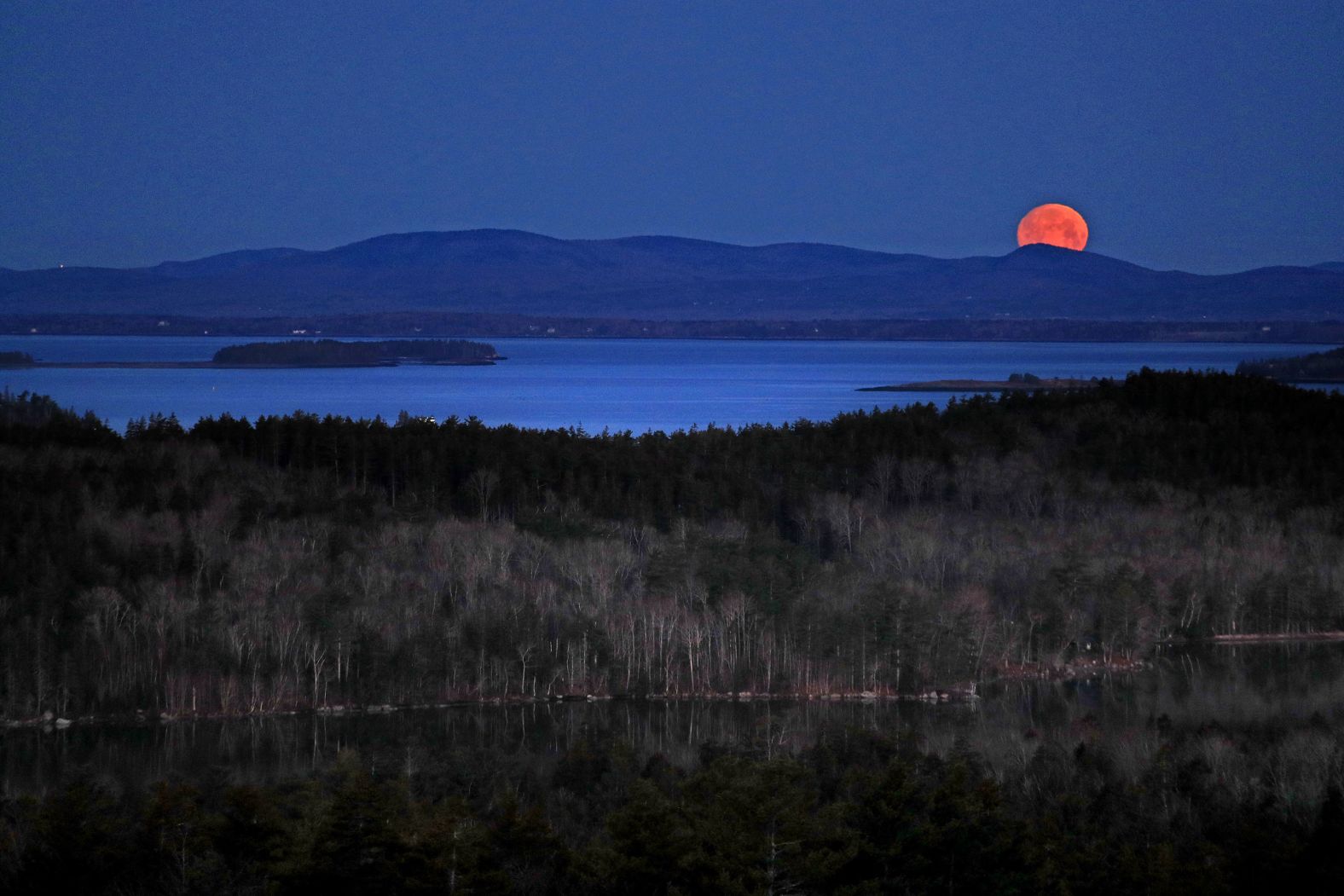 The moon peeks out behind the Camden Hills in Camden, Maine.