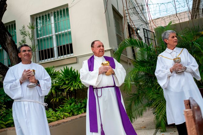 From left, minister Ismael Fletcher, Monsignor Jose Emilio Cummins and minister Eva Pilar Garcia wait in front of a parish in San Juan, Puerto Rico, during a drive-thru communion on March 21.