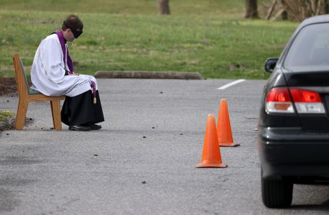 The Rev. Scott Holmer offers a drive-thru confessional March 20 in the parking lot of St. Edward the Confessor Catholic Church in Bowie, Maryland. Holmer sits 6 feet away from cars as people pull up to talk to him.