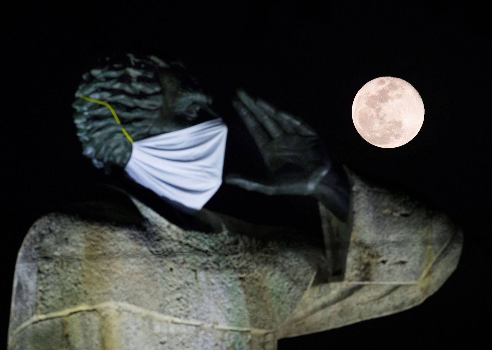 The moon rises behind the statue of priest Antonio Montesino wearing a face mask in Santo Domingo, Dominican Republic.