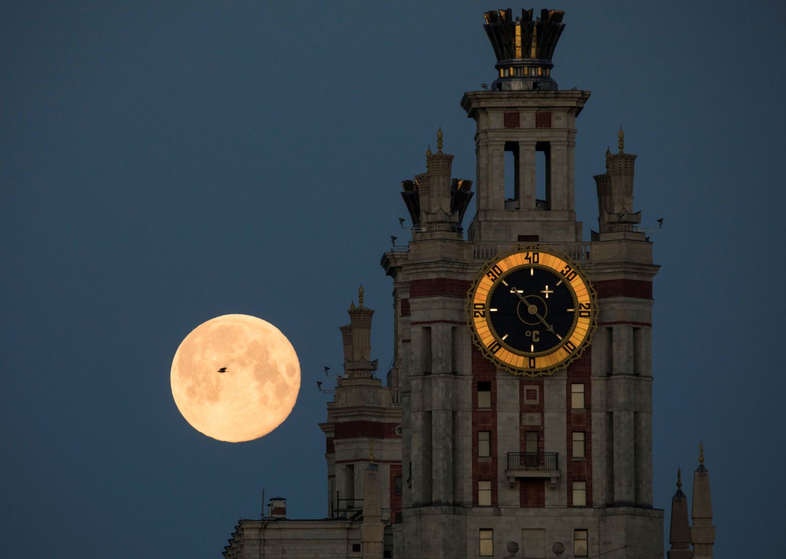 A bird flies past the moon, which is seen behind Moscow State University on Friday, May 8.