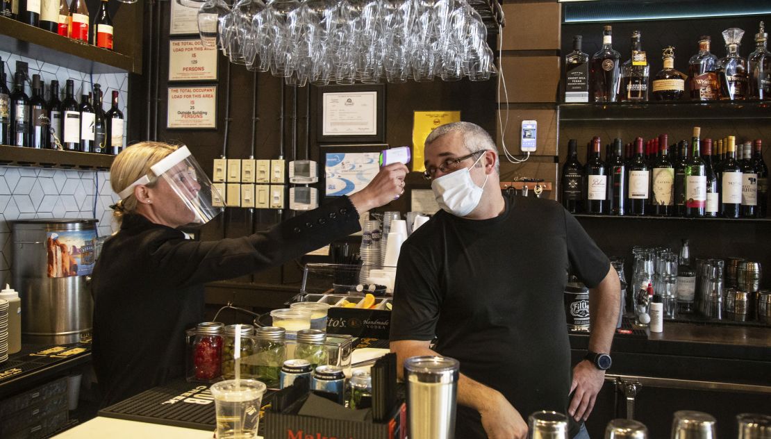 Tavern owner Jenna Aronowitz takes the temperature of bartender Shane Goode before the restaurant opens for sit down meals in Brookhaven, Ga.