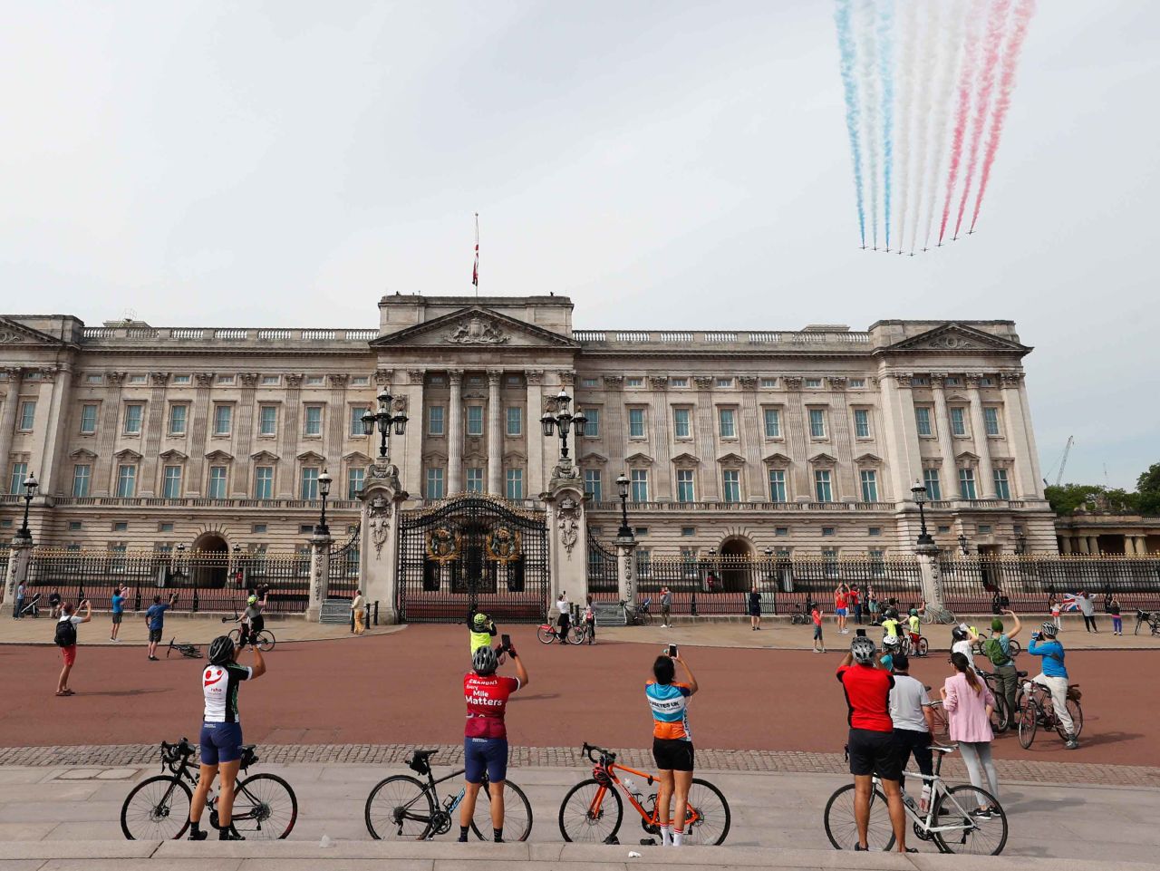 Cyclists watch as the Red Arrows fly over Buckingham Palace in London.