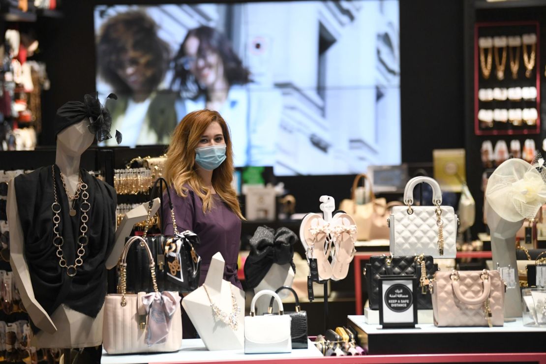 A vendor, wearing a mask for protection against the coronavirus, stands next to handbags at a shop in Dubai Mall. 