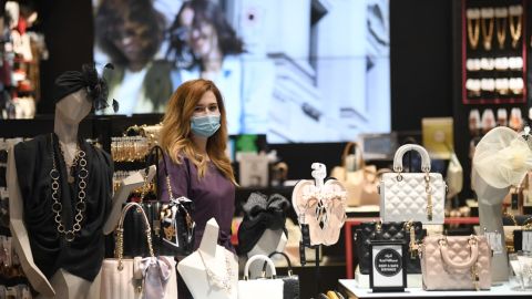 A vendor, wearing a mask for protection against the coronavirus, stands next to handbags at a shop in Dubai Mall. 