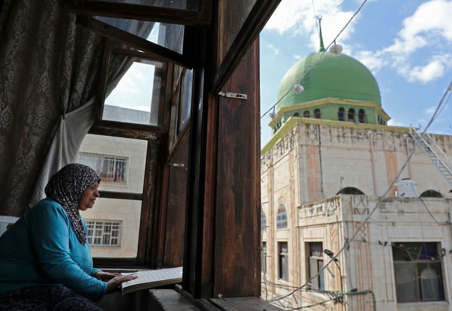 A woman reads the Quran at her window overlooking the Al-Nasr Mosque in Nablus, West Bank, on May 10.