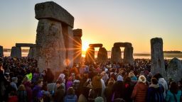 The sun rises between the stones and over crowds at Stonehenge where people gather to celebrate the dawn of the longest day in the UK.