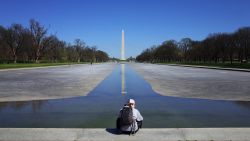A man sits on the edge of the Reflecting Pool which has been drained for maintenance on the Mall in Washington, DC on March 26, 2020. - After days of negotiations, the Senate has passed a historic $2.2 trillion plan to stimulate the US economy as it faces soaring unemployment and recession caused by the coronavirus pandemic. (Photo by Mandel Ngan/AFP/Getty Images)