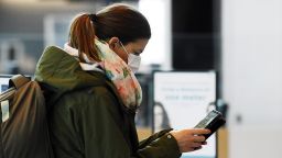 A passenger, wearing a face mask, looks at her phone at the Helsinki International Airport in Vantaa, Finland, on May 13, 2020. - The Finnish airport operator Finavia requires the use of mouth-nose protectors of all airport employees who work in the customer interface. It also strongly recommends that passengers use a mask as they move about the airport. (Photo by Vesa Moilanen/AFP/Getty Images)