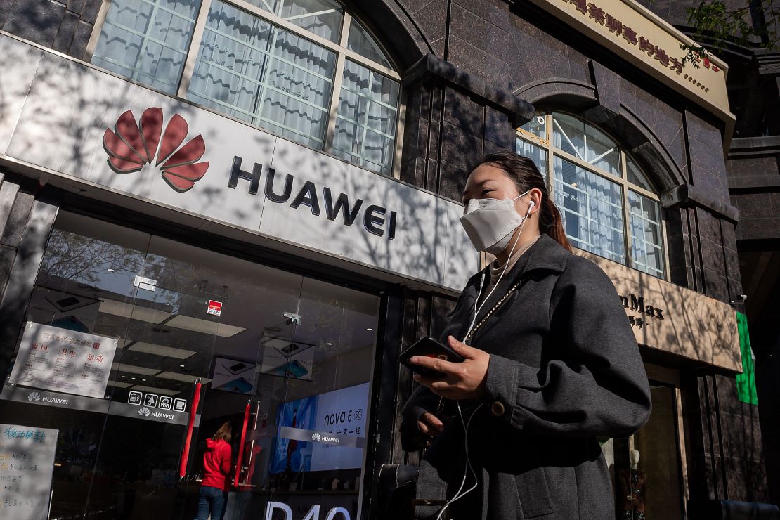 A woman wearing a face mask amid concerns over the Covid-19 coronavirus walks holding her smartphone past a Huawei shop (L) on a street in Beijing on April 22, 2020. 