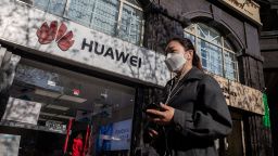 A woman wearing a face mask amid concerns over the COVID-19 coronavirus walks holding her smartphone past a Huawei shop (L) on a street in Beijing on April 22, 2020. - China's economy shrank for the first time in decades last quarter as the coronavirus paralysed the country, in a historic blow to the Communist Party's pledge of continued prosperity in return for unquestioned political power. (Photo by Nicolas Asfouri/AFP/Getty Images)