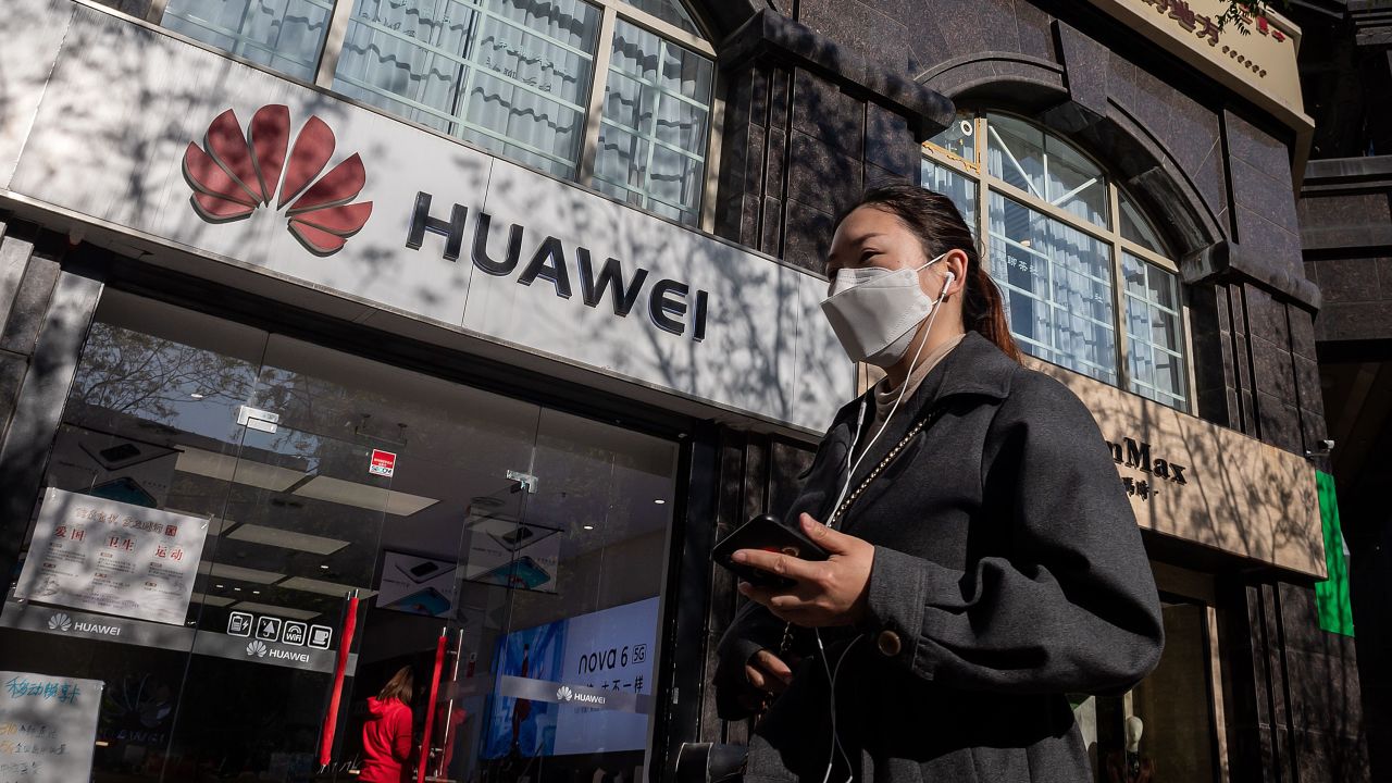 A woman wearing a face mask amid concerns over the Covid-19 coronavirus walks holding her smartphone past a Huawei shop (L) on a street in Beijing on April 22, 2020.