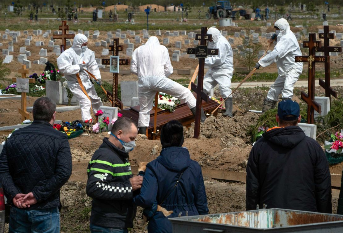 Grave diggers bury a COVID-19 victim as relatives and friends stand at a safe distance, at a cemetary in Kolpino, outside St. Petersburg, on Friday.