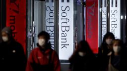 Pedestrians wearing protective masks walk past illuminated signage forSoftBank Corp. and the company's Y!mobile brand displayed outside a store at night in Tokyo, Japan, on Tuesday, April 14, 2020.