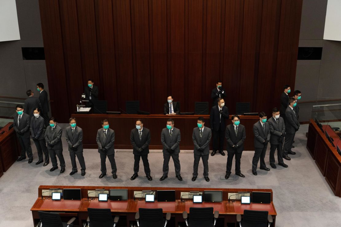 Chan Kin-por is surrounded by security officers as he sits in the chairperson's seat.