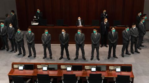 Chan Kin-por is surrounded by security officers as he sits in the chairperson's seat.