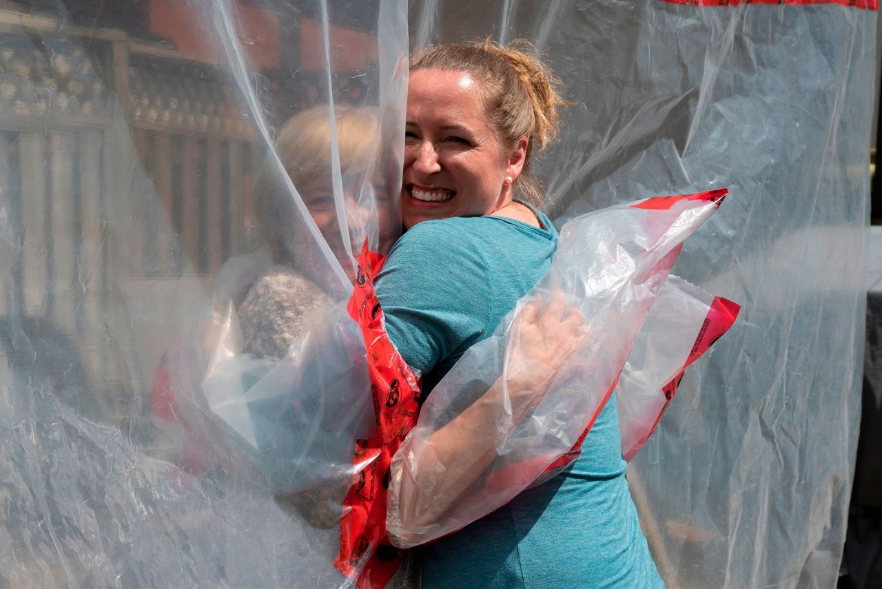 Carolyn Ellis, right, hugs her mother, Susan Watts, in Guelph, Ontario, on May 16. They're avoiding direct contact by using the "hug glove" that Carolyn and her husband, Andrew, created as a Mother's Day gift. It features a plastic tarp with four sleeves attached to a clothesline.