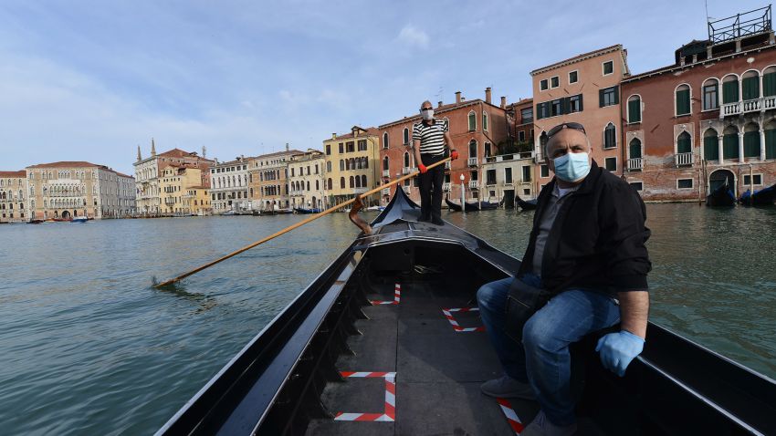 TOPSHOT - A gondolier wearing a face mask (Rear) transports his very first customer as service resumes at the San Toma embankment on a Venice canal on May 18, 2020 during the country's lockdown aimed at curbing the spread of the COVID-19 infection, caused by the novel coronavirus. - Restaurants and churches reopen in Italy on May 18, 2020 as part of a fresh wave of lockdown easing in Europe and the country's latest step in a cautious, gradual return to normality, allowing businesses and churches to reopen after a two-month lockdown. (Photo by ANDREA PATTARO / AFP) (Photo by ANDREA PATTARO/AFP via Getty Images)