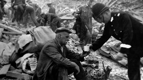 A British police officer hands a victim tea in the middle of the  bombing wreckage during World War II. 
