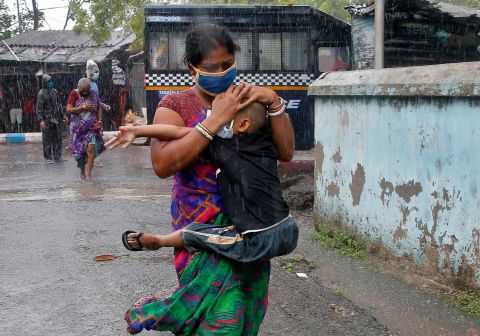 A woman carries a child through heavy rain as they evacuate a slum in Kolkata on May 20.