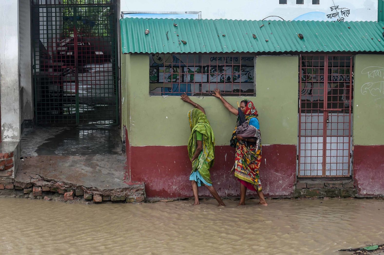 Residents walk along a house on a flooded street in Dacope.