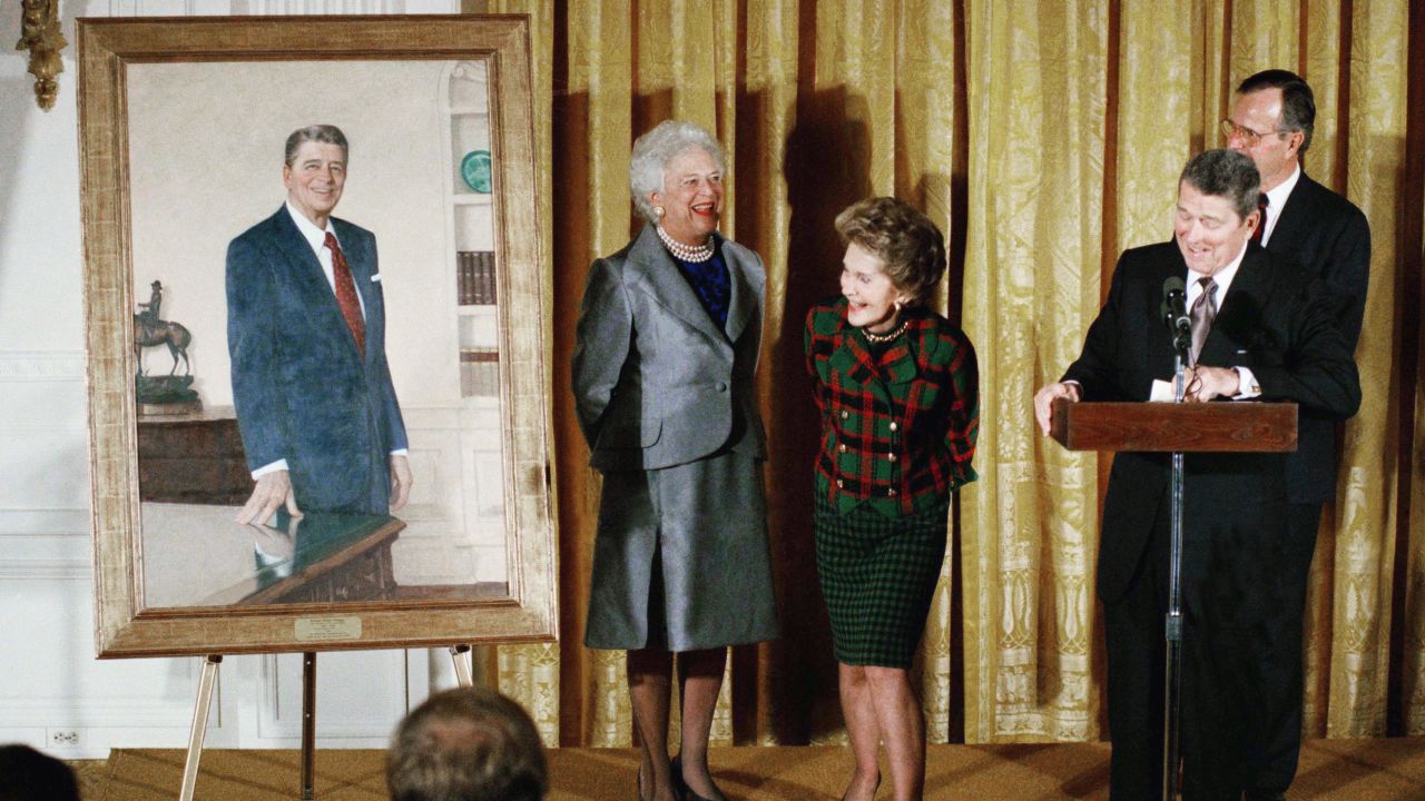Former President Ronald Reagan and former first lady Nancy Reagan take a peek at a portrait of the former president along with then-President George H.W. Bush and then-first lady Barbara Bush during an unveiling ceremony at the White House in November 1989. 