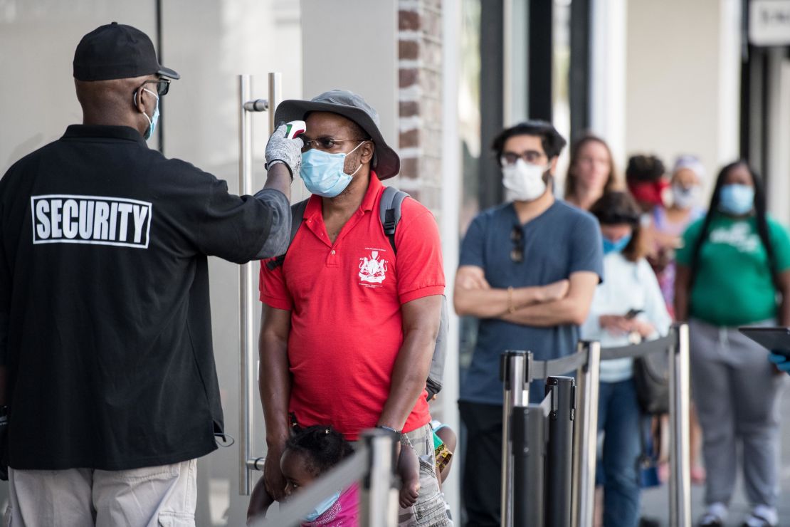A security guard takes a customer's temperature outside an Apple Store in South Carolina. The responsibilities of retail security guards have changed during the pandemic.