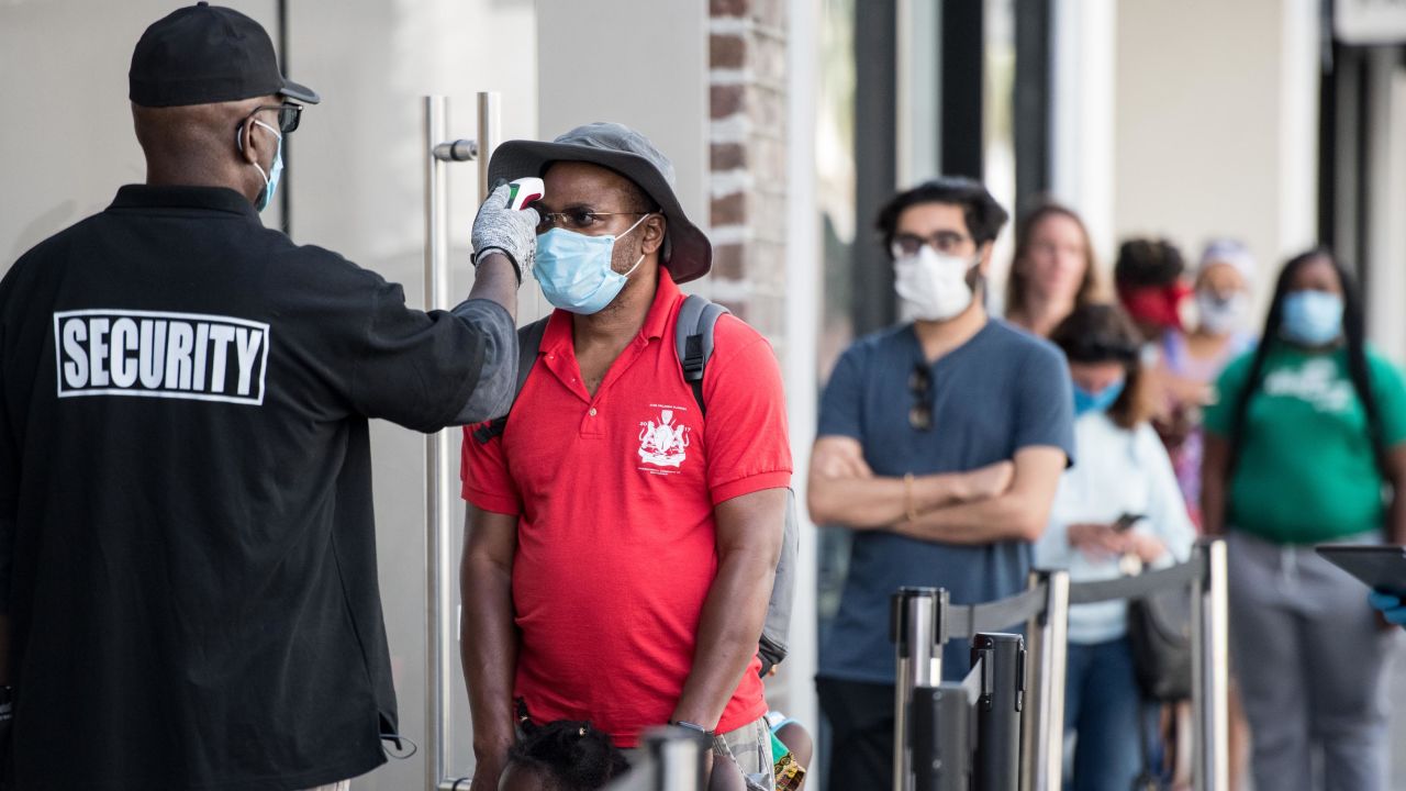 A security guard takes a customer's temperature outside an Apple Store in South Carolina. The responsibilities of retail security guards have changed during the pandemic.