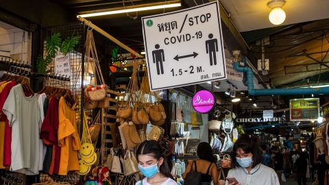 Shoppers wearing face masks walk past a sign reminding visitors to observe social distancing at Bangkok's Chatuchak Weekend Market on May 17.