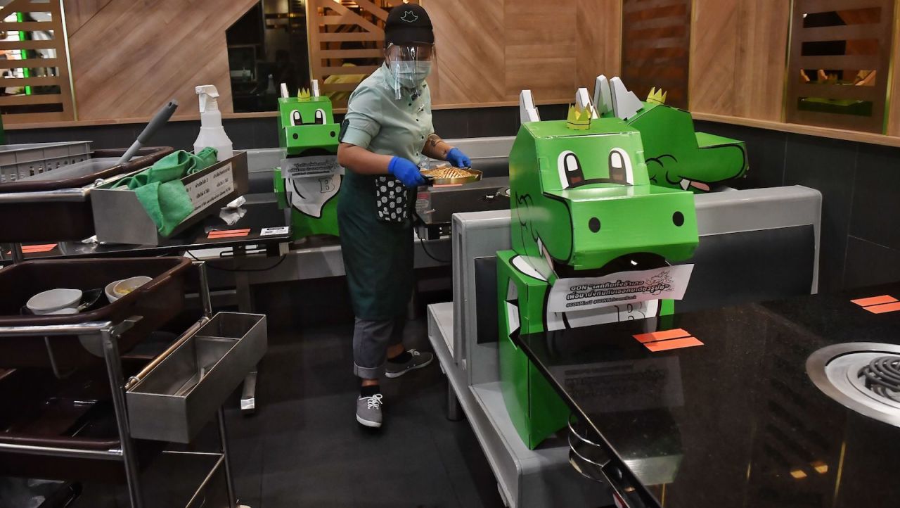 <strong>IconSiam: </strong>A waiter clears a hotpot next to cardboard dinosaurs used for social distancing at Bar-B-Q Plaza, a popular Thailand restaurant chain, at the IconSiam luxury shopping mall on May 17, 2020.  