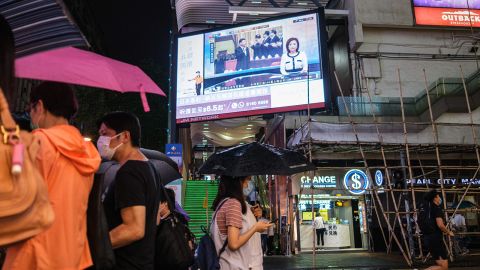 Pedestrians walk under a television screen in Hong Kong on May 21, 2020, showing a news broadcast of footage from Beijing of Chinese President Xi Jinping (C) at the Chinese People's Political Consultative Conference.
