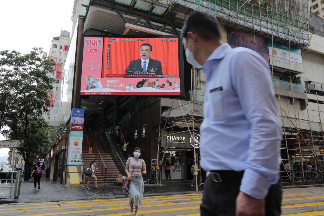 Pedestrians in Hong Kong wearing protective masks walk past a screen playing a news report on Chinese Premier Li Keqiang speaking at the National People's Congress on Friday.