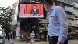 Pedestrians wearing protective masks walk past a screen playing a news report on Chinese Premier Li Keqiang speaking at the National People's Congress in Hong Kong, China, on Friday, May 22, 2020.