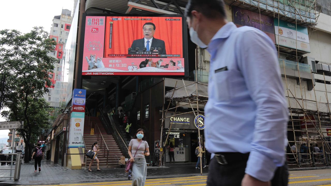 Pedestrians in Hong Kong wearing protective masks walk past a screen playing a news report on Chinese Premier Li Keqiang speaking at the National People's Congress on Friday.
