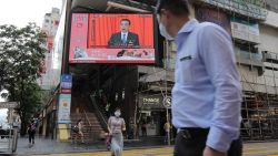 Pedestrians wearing protective masks walk past a screen playing a news report on Chinese Premier Li Keqiang speaking at the National People's Congress in Hong Kong, China, on Friday, May 22, 2020. Democracy advocates called for protests against sweeping national security legislation China introduced Friday, as authorities in Beijing vowed to end what they called a "defenseless" posture due to "those trying to sow trouble." Photographer: Paul Yeung/Bloomberg via Getty Images