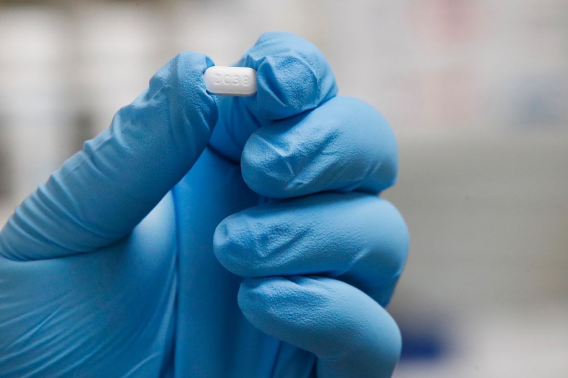 A pharmacy tech holds a pill of hydroxychloroquine.