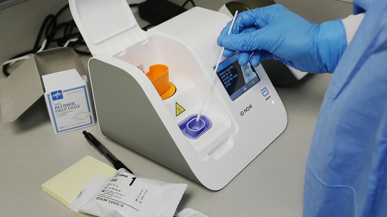 A lab technician dips a sample into the Abbott Laboratories ID Now testing machine at the Detroit Health Center. 