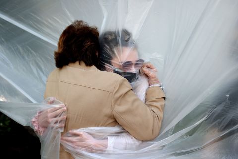 Olivia Grant, right, hugs her grandmother, Mary Grace Sileo, through a plastic drop cloth that was hung up on a homemade clothesline in Wantagh, New York.