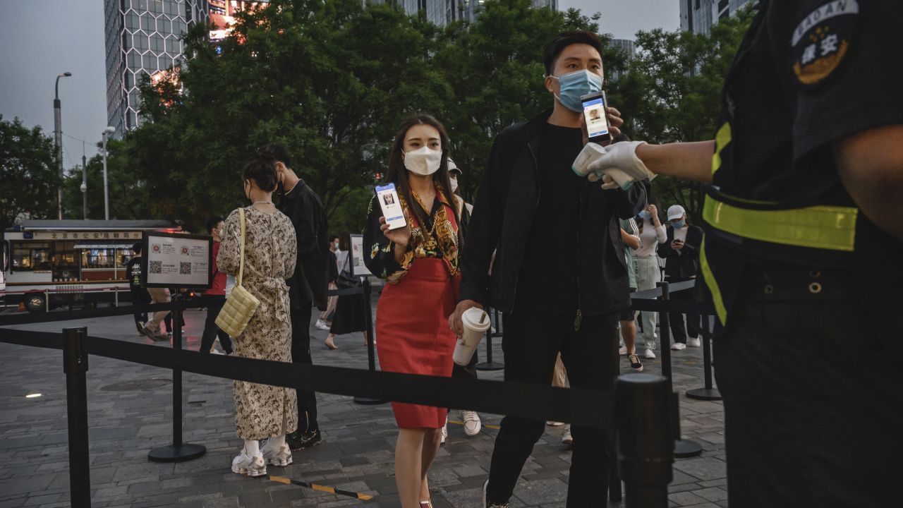 A Chinese man and woman in Beijing show their local health QR codes to a security guard as he checks her temperature before entering a shopping area on May 3.