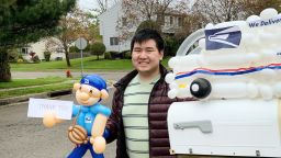 22-year-old balloon artist Eddie Lee of Edison, New Jersey is making balloon sculptures for essential workers. He poses here with artwork he made for his local postal carrier.