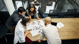 A team of young people in a modern office is discussing their project. The group consists of two men and two women, the are seen in bird's eye view.